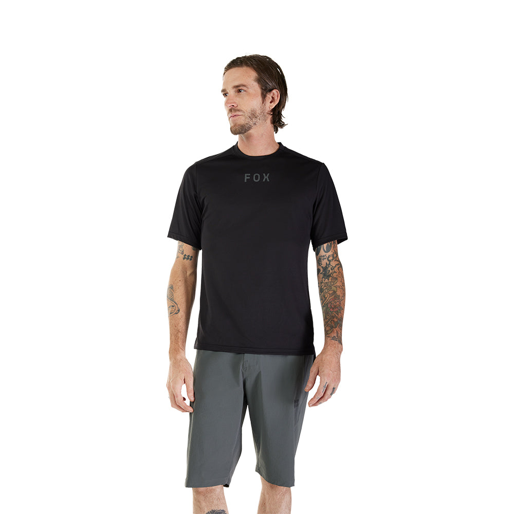 Man wearing a black t-shirt with 'FOX' logo and gray shorts on a white background