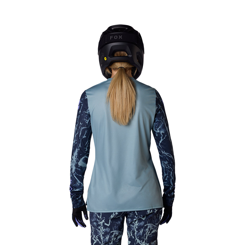 Person wearing a light blue long-sleeve top with dark blue patterns, black helmet, and gloves on a white background.