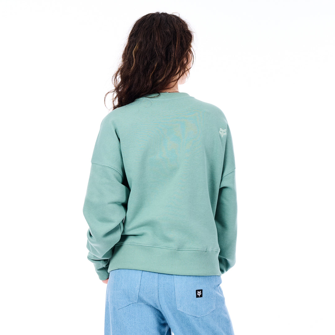 Person wearing a light green sweatshirt with a logo on the back, standing against a white background.
