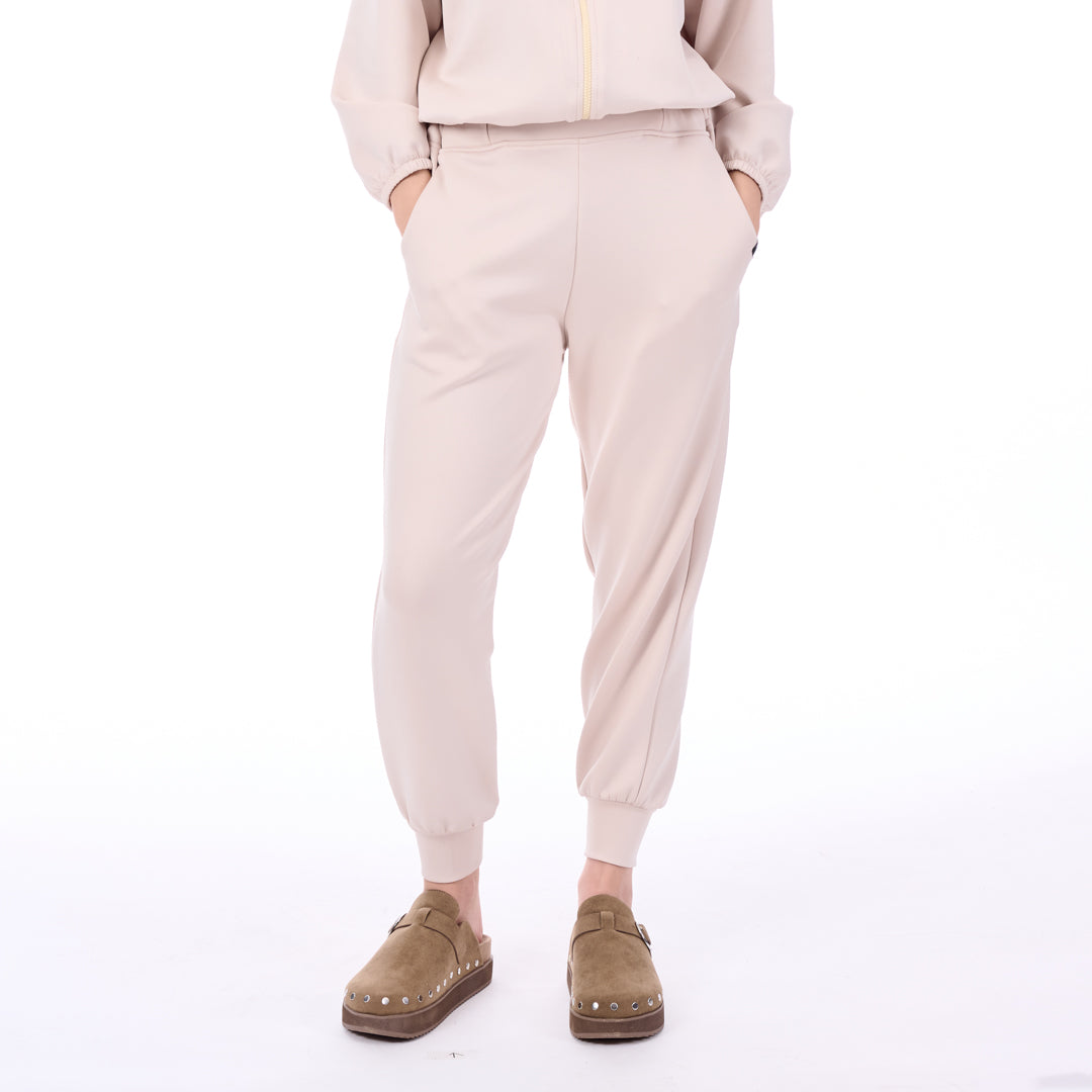 Person wearing beige jogger pants and brown shoes on a white background