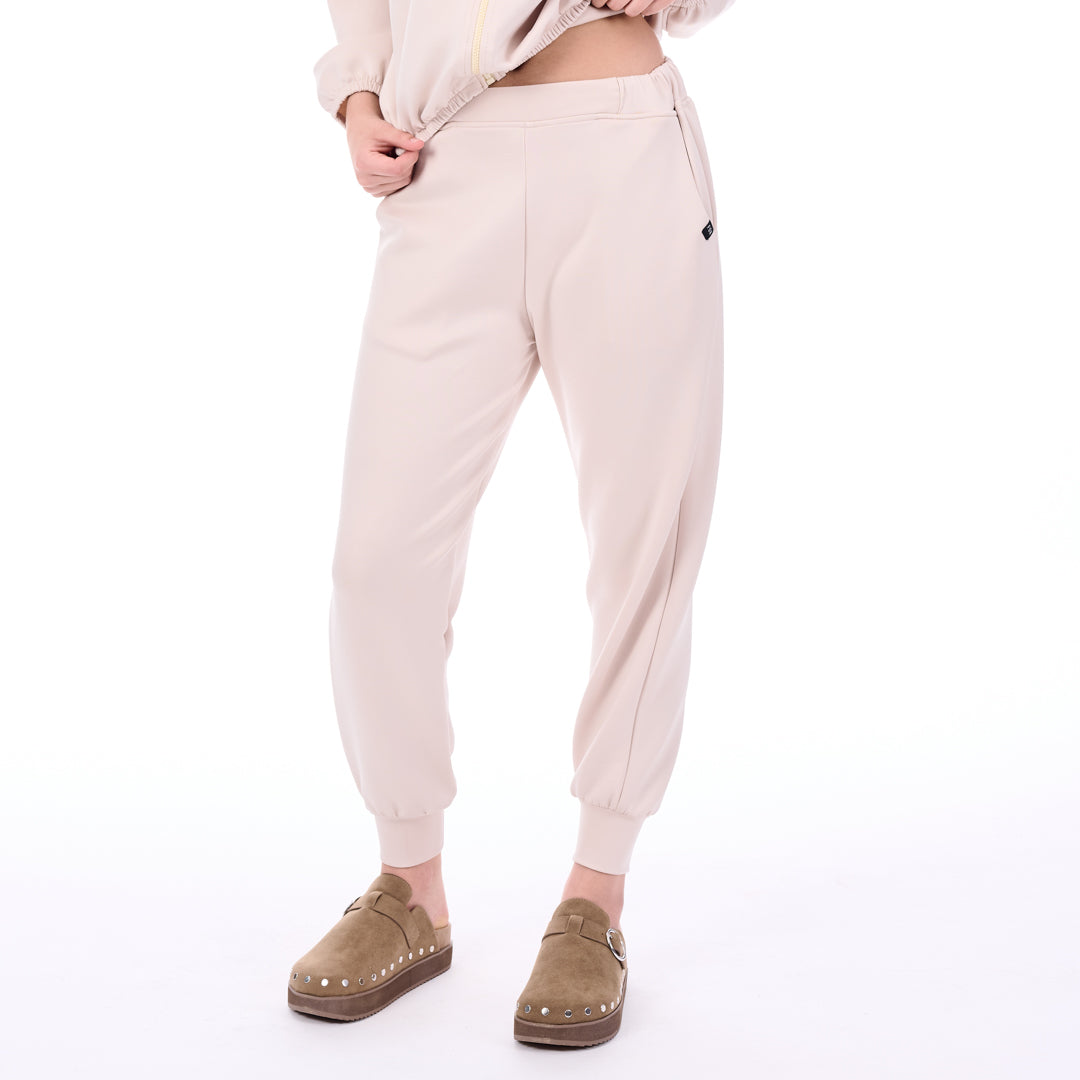 Person wearing light pink jogger pants and brown shoes on a white background